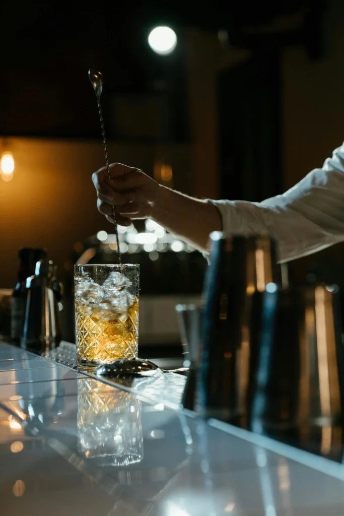 Bartender stirring a cocktail with ice in a crystal glass at a bar counter.