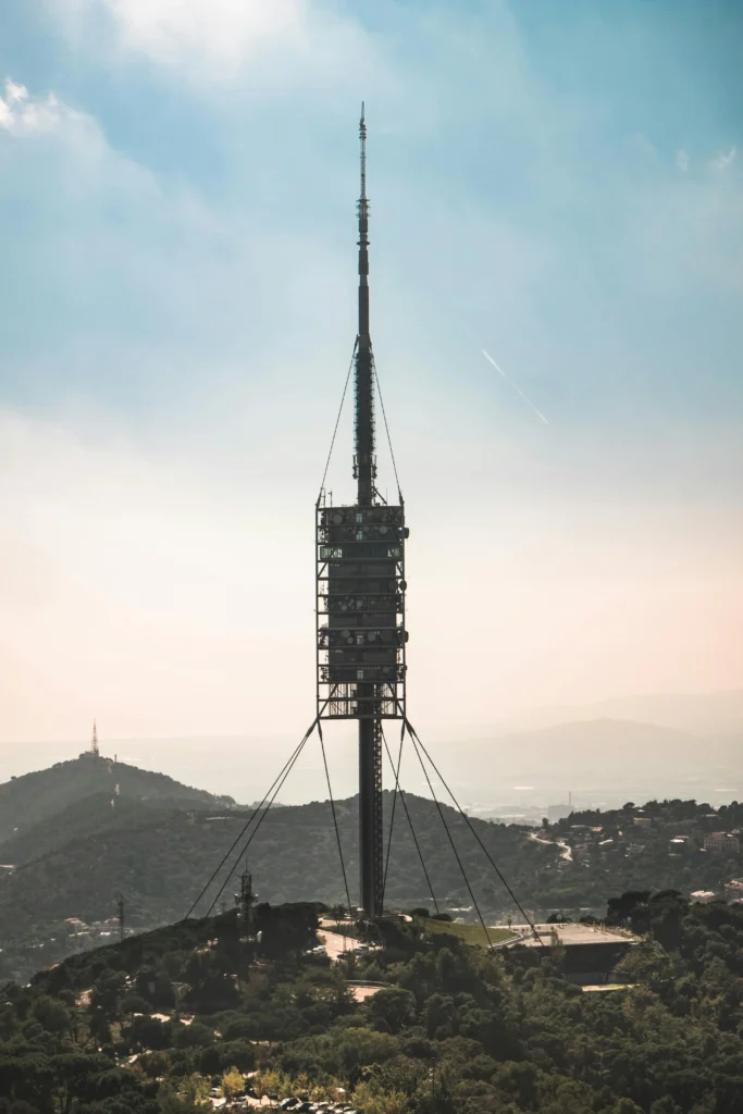 Torre de Collserola communications tower in Barcelona, surrounded by green hills with a hazy city backdrop.