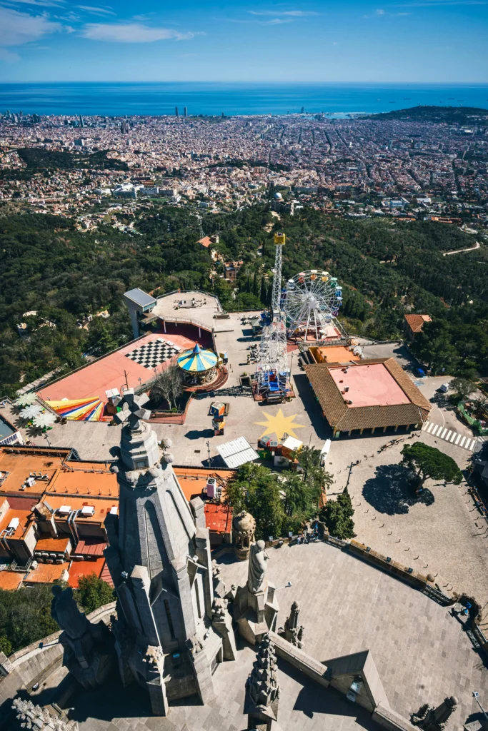 Aerial view of Tibidabo Amusement Park with colorful rides, Ferris wheel, and panoramic view of Barcelona and the Mediterranean Sea.