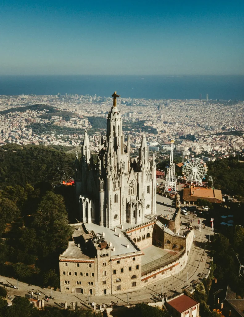 Aerial view of the Temple Expiatori del Sagrat Cor on Mount Tibidabo in Barcelona, with the city and sea in the background.