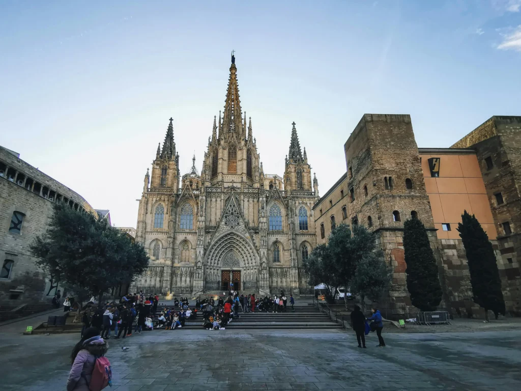 Vista frontal de la Catedral de Barcelona en el Barrio Gótico con turistas en la plaza al atardecer