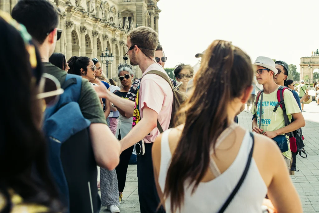 Un grupo de turistas escucha atentamente a un guía con micrófono durante un tour guiado en una plaza histórica de la ciudad, frente a un edificio monumental.