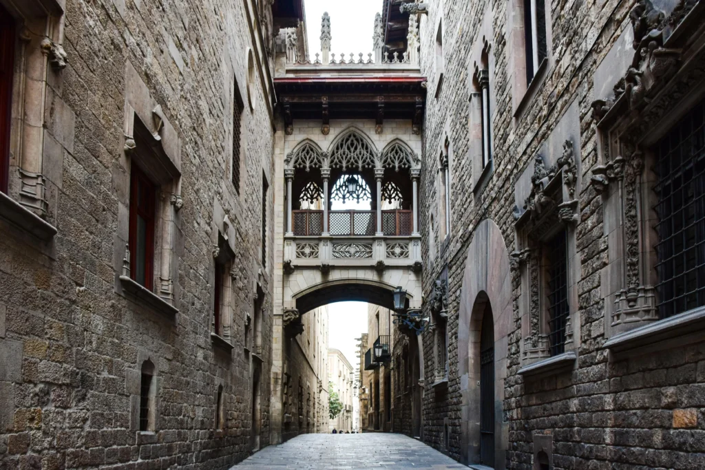 Vista del Puente del Obispo en el Barrio Gótico de Barcelona, un pasaje gótico que conecta dos edificios históricos sobre una calle estrecha de piedra.