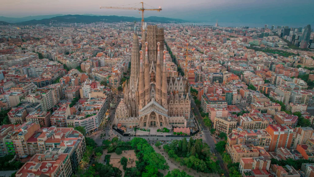 Imagen aérea de la Sagrada Familia en el centro de Barcelona, rodeada de edificios y con una grúa visible en su construcción.