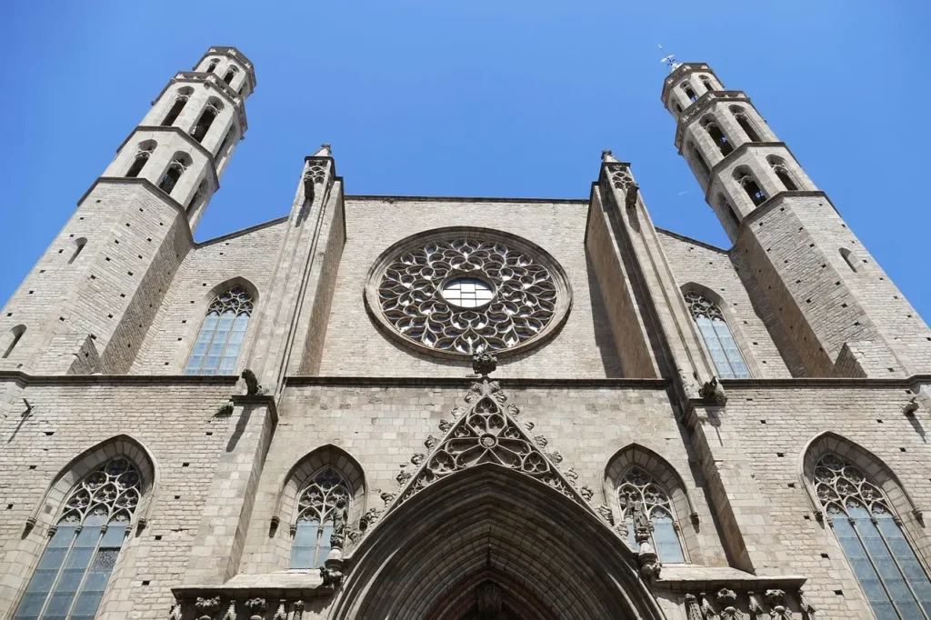 Vista en contrapicado de la fachada gótica de la Basílica de Santa María del Mar en Barcelona, con sus dos torres y el rosetón central bajo un cielo despejado.