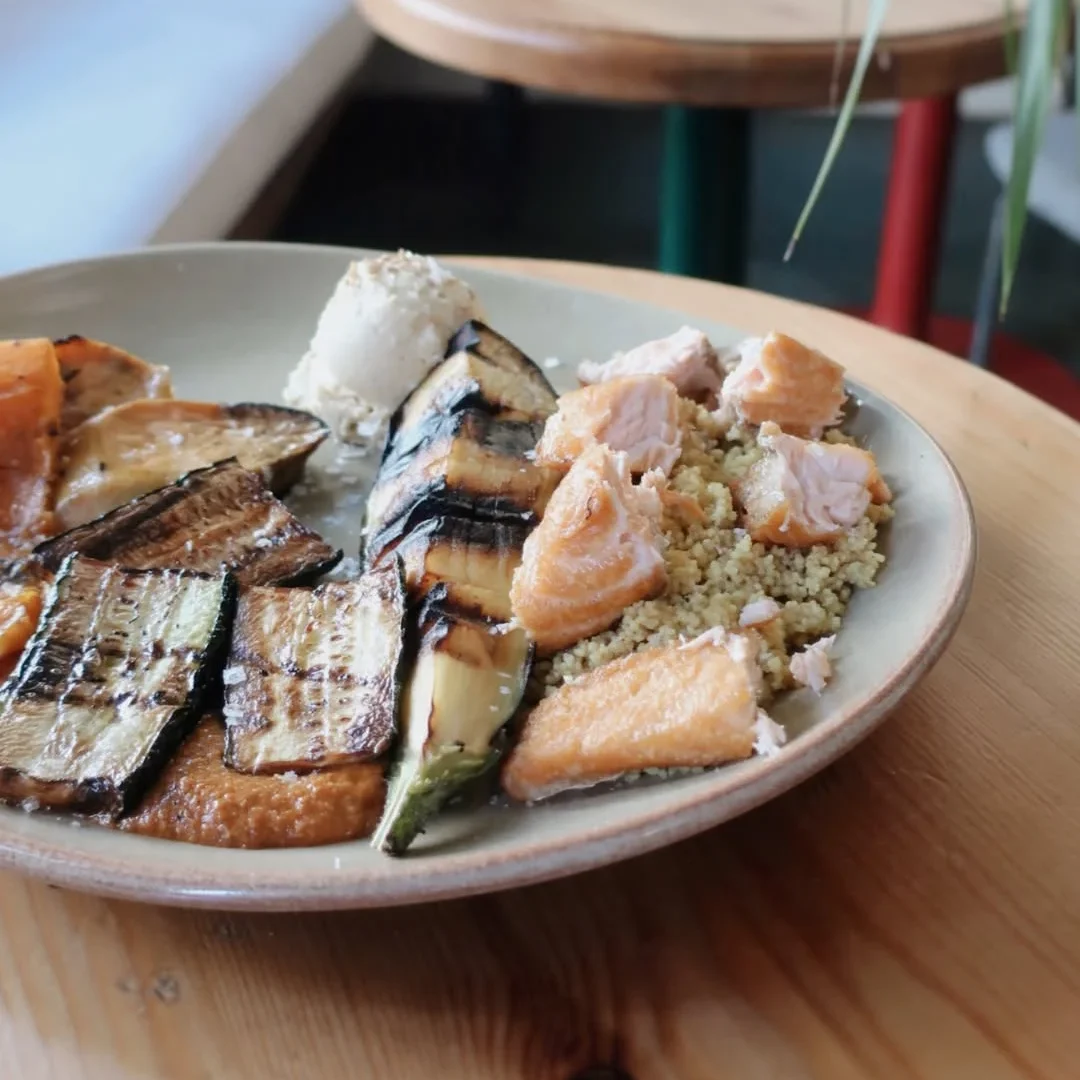 A nourishing plate with grilled zucchini and eggplant, salmon chunks, quinoa, and hummus, served in a relaxed dining atmosphere.