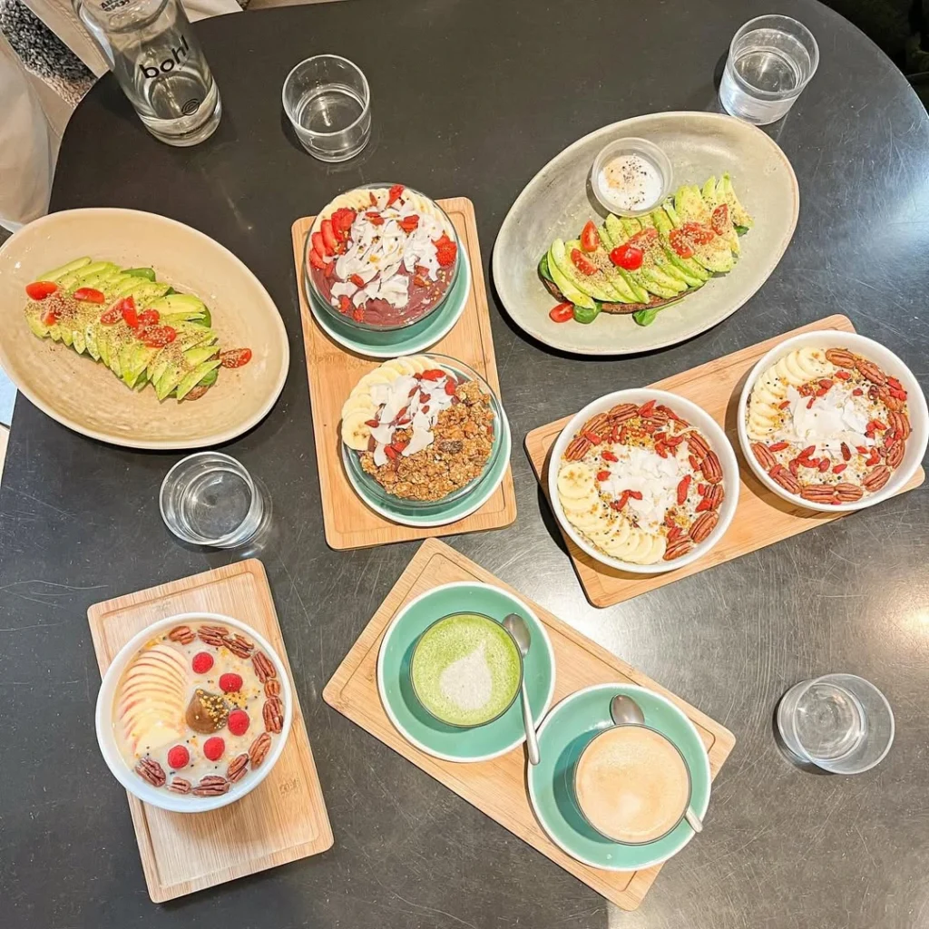 A table set with a variety of colorful smoothie bowls, avocado toasts, and hot beverages