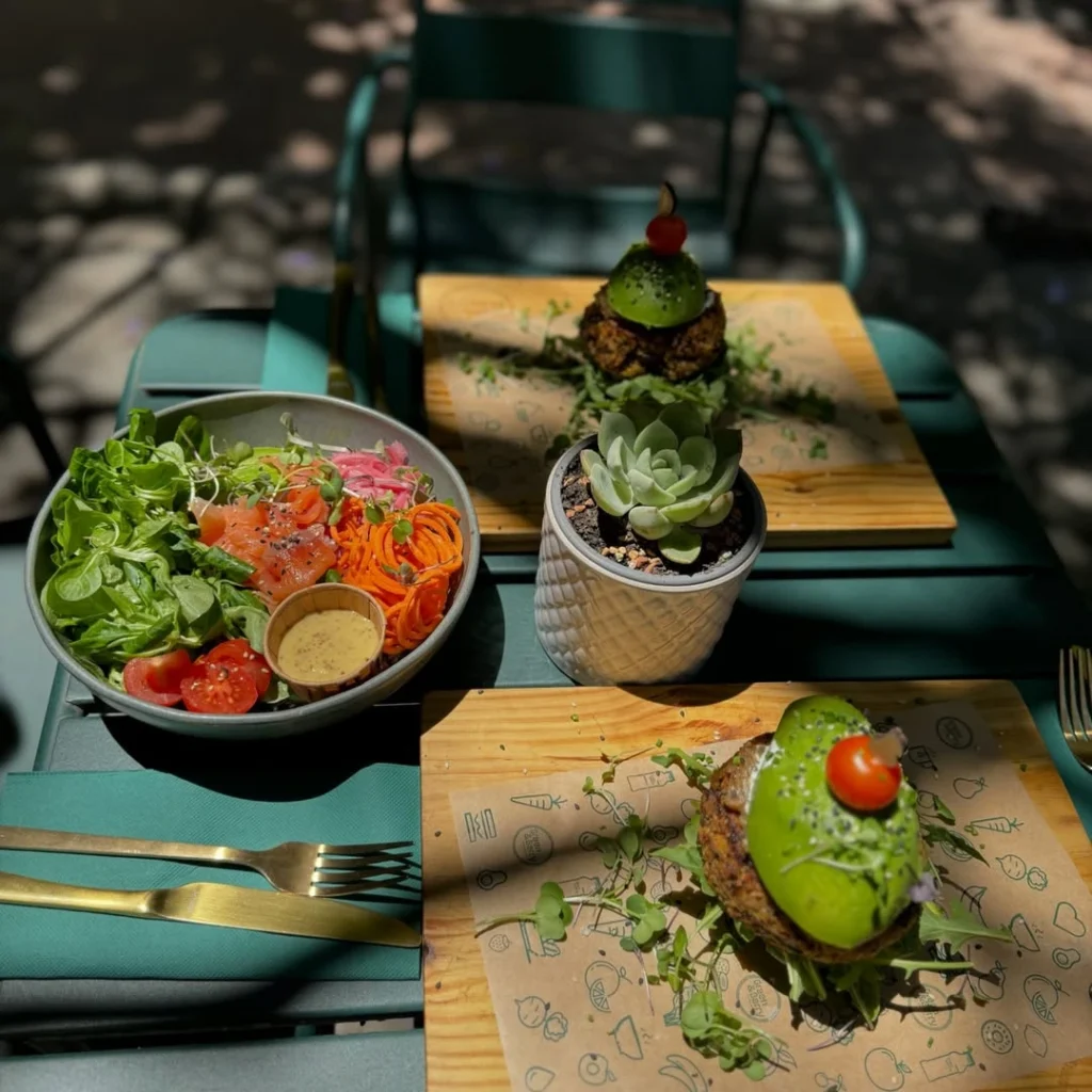 A green vegan burger and a fresh salad served on a wooden tray at an outdoor café.