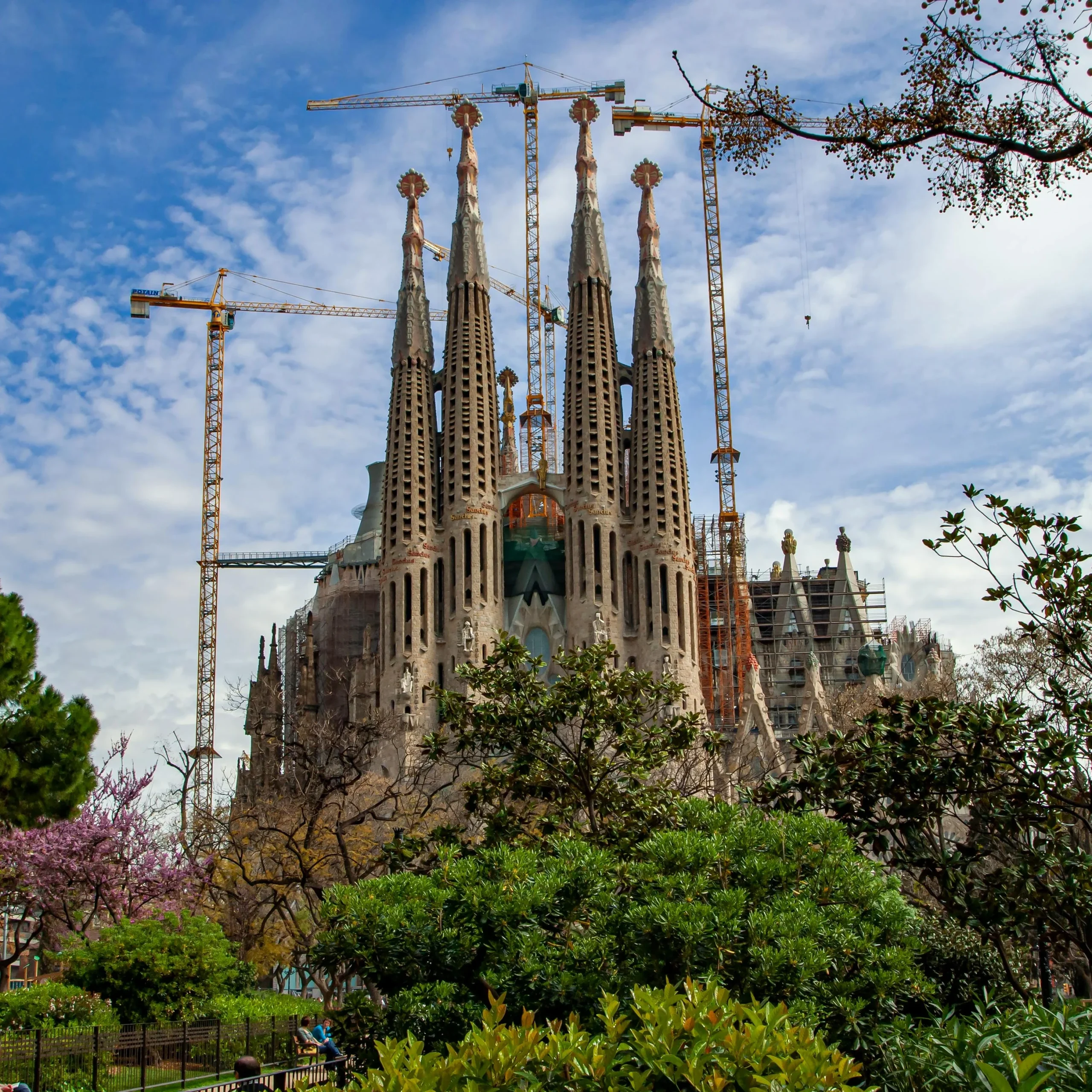 The iconic Sagrada Familia in Barcelona, surrounded by lush greenery and construction cranes in the background.