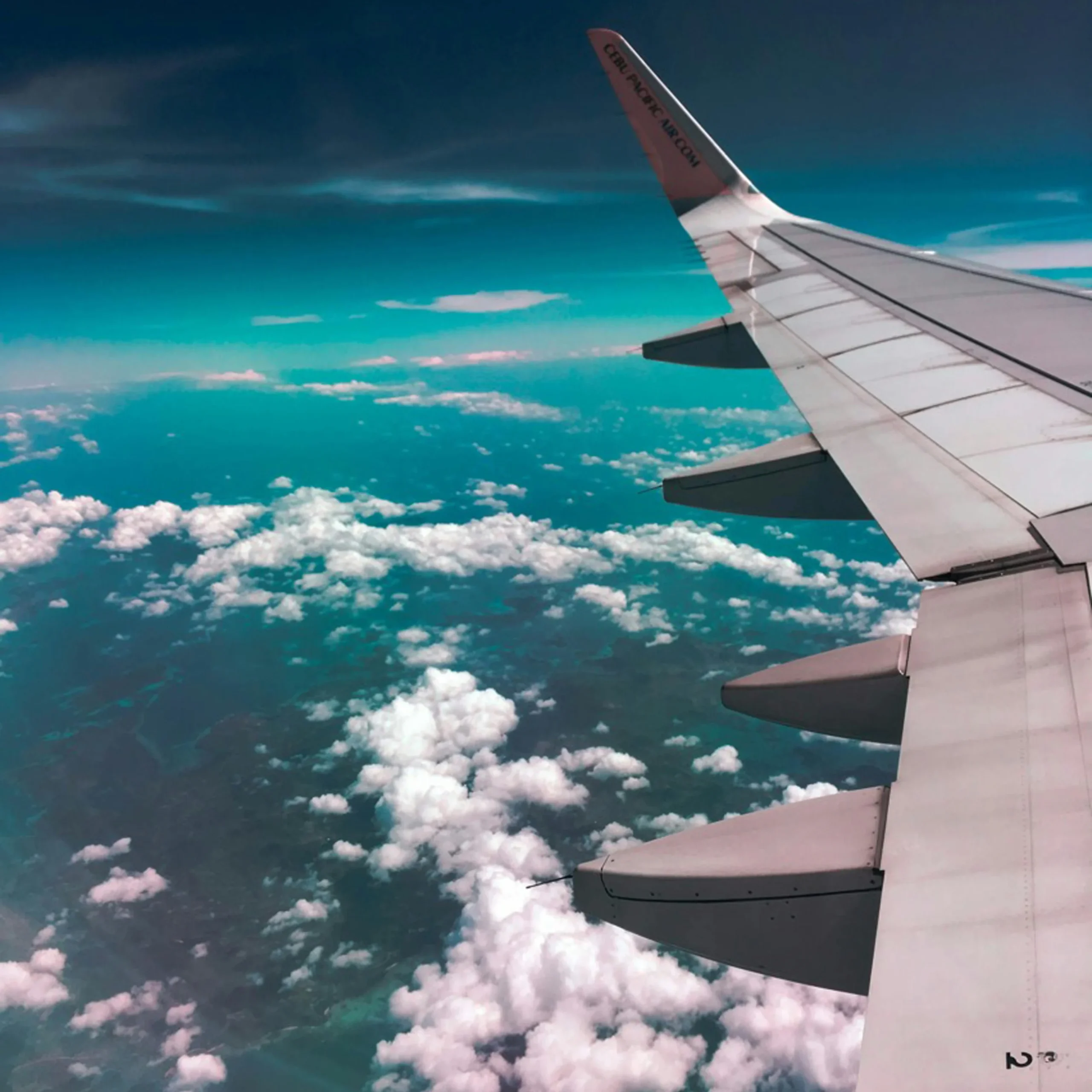 A breathtaking aerial view from an airplane window, showing fluffy white clouds and a sleek wing against the sky.