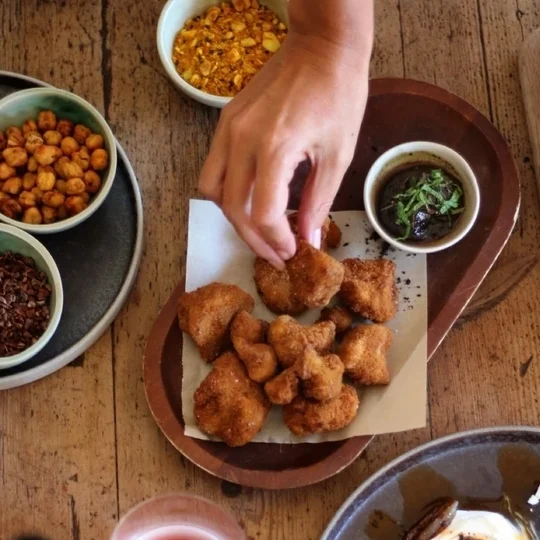 A rustic wooden table with a selection of tapas, including crispy fried bites, dipping sauces, and roasted vegetables, perfect for sharing.