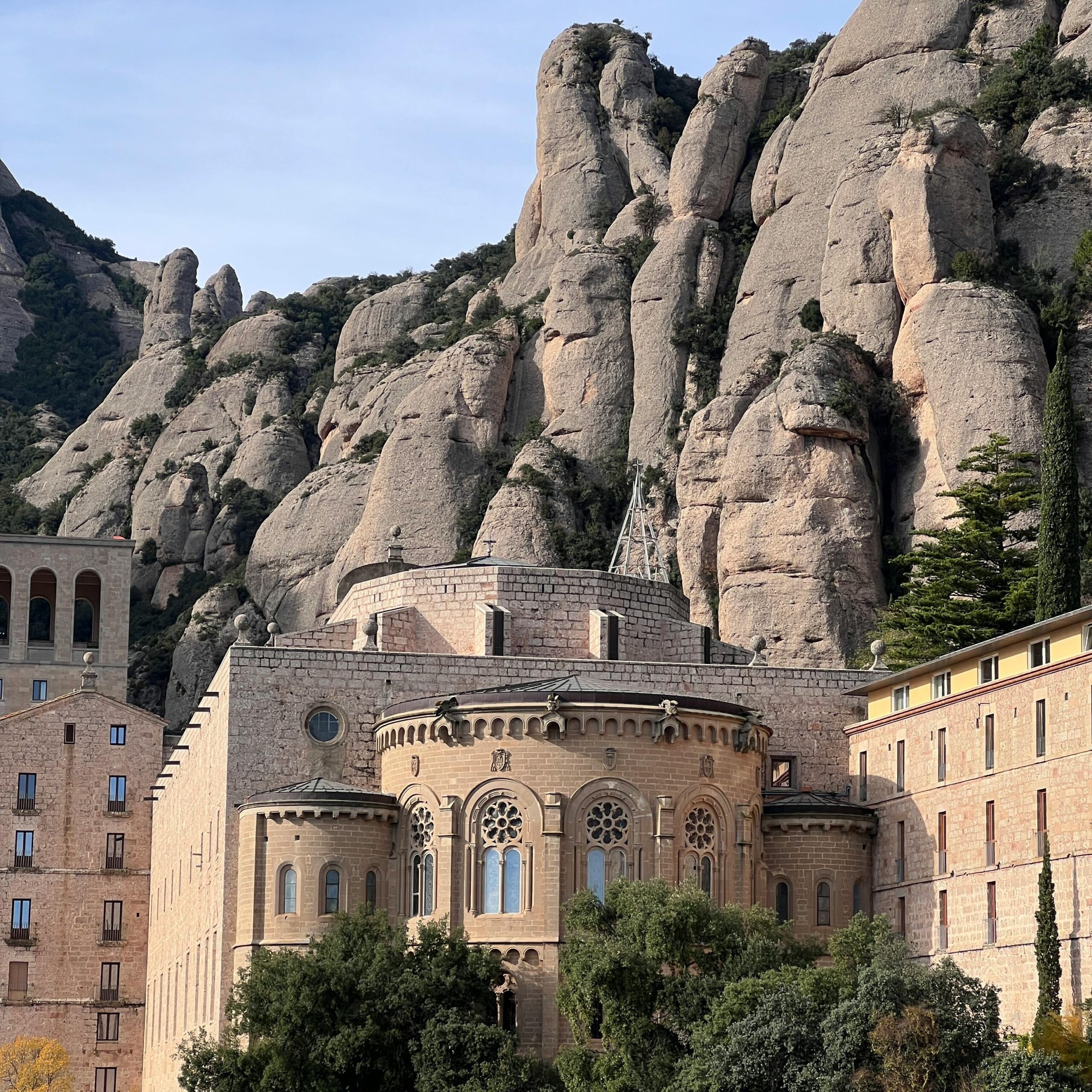 The Montserrat Monastery, nestled at the base of the dramatic Montserrat mountain range in Catalonia, Spain. The monastery's distinct architecture stands against the backdrop of towering, jagged rock formations and lush greenery, creating a serene and picturesque landscape