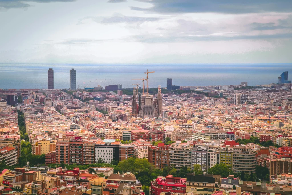 A panoramic view of Barcelona with the Sagrada Família in the center, the Mediterranean Sea in the background, and the city’s skyline with modern and historic buildings.