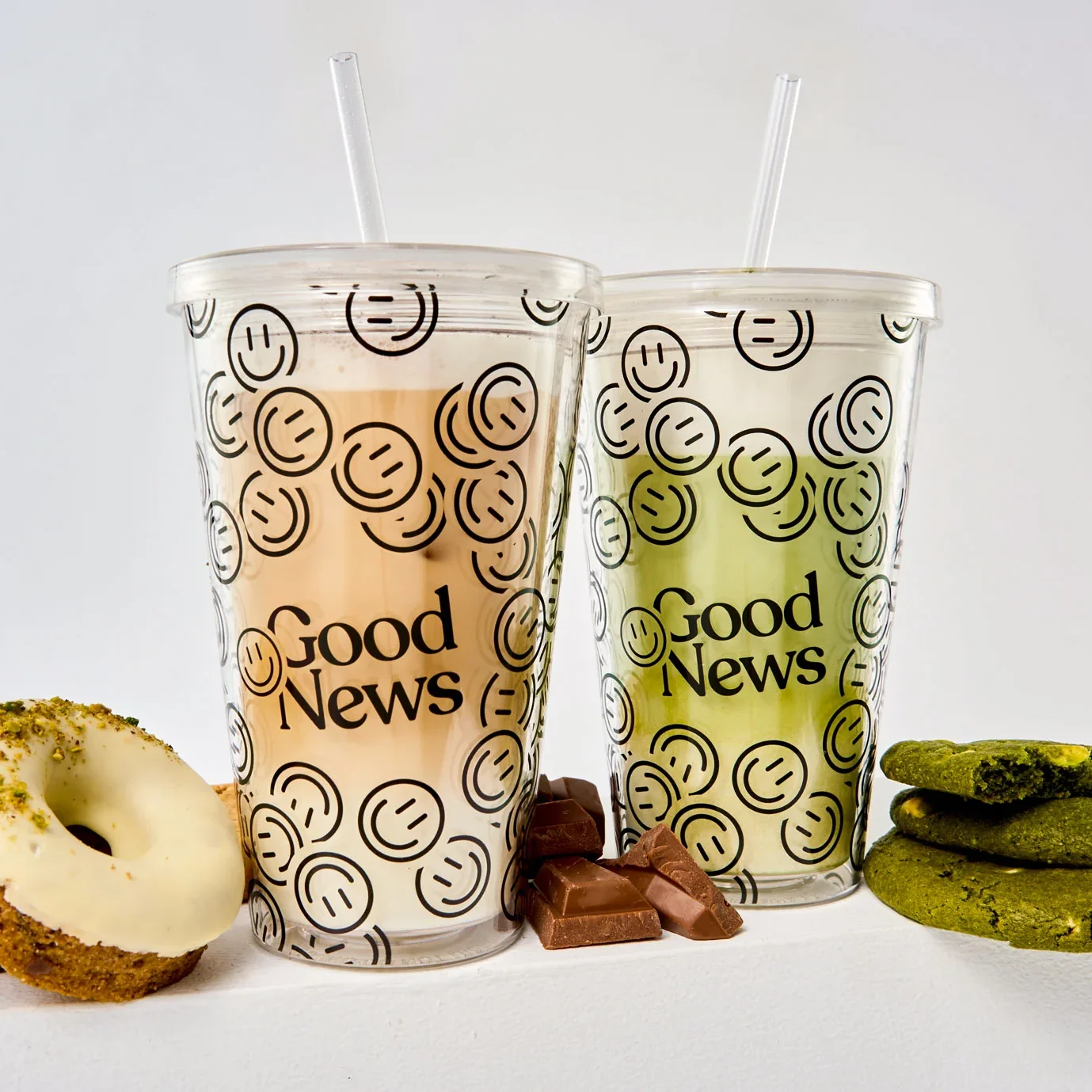 Eiskaffee und Matcha von Good News Coffee in Barcelona, serviert in Bechern mit Smiley-Logo, dazu Donuts, Milchschokolade und Matcha-Kekse.