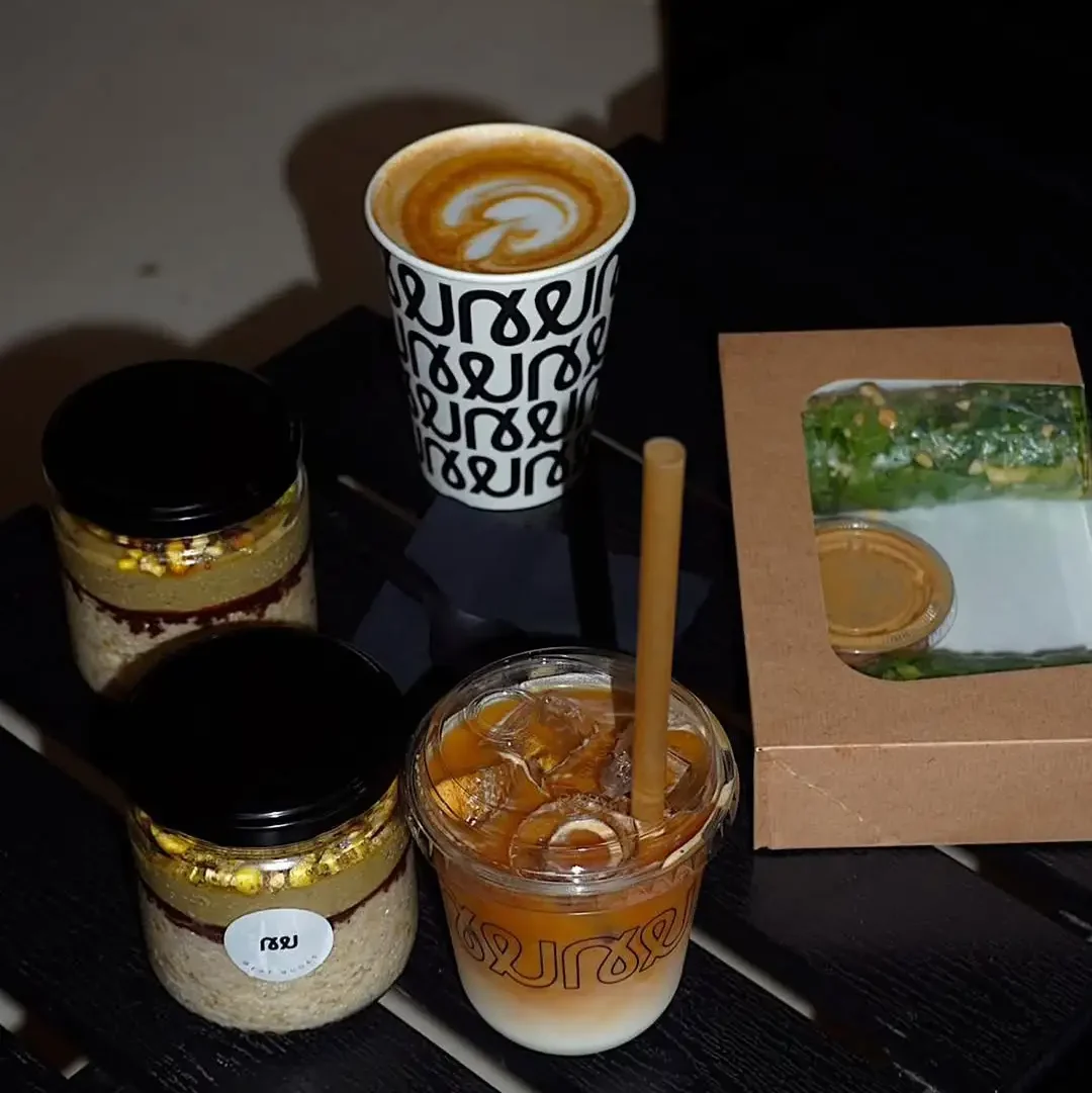 Eiskaffee, Cappuccino und Gläser mit Overnight Oats vom Nudes Coffee Shop in Barcelona, serviert auf einem schwarzen Tisch mit einem Take-away-Salat.