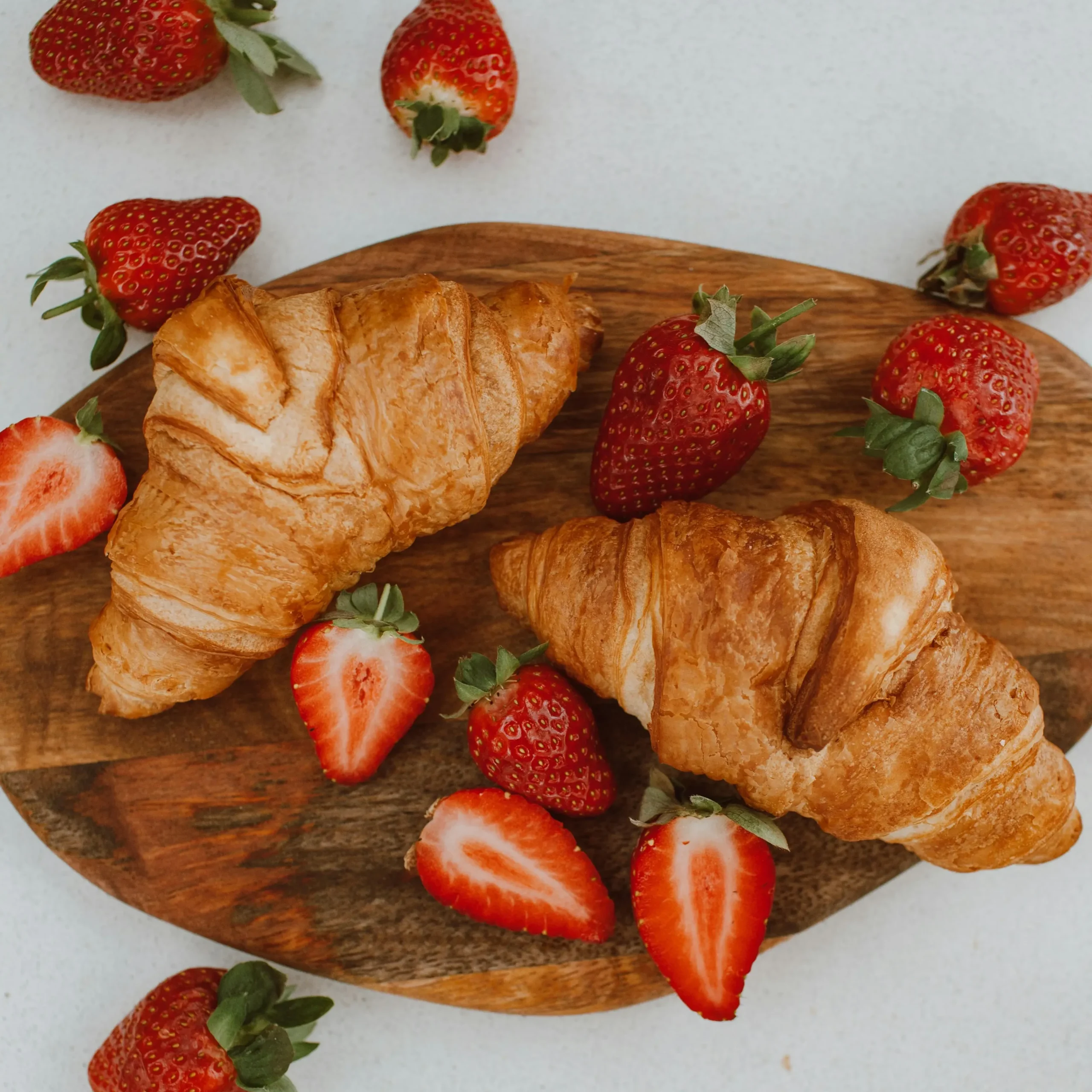 Fresh buttery croissants served with ripe strawberries on a wooden board.