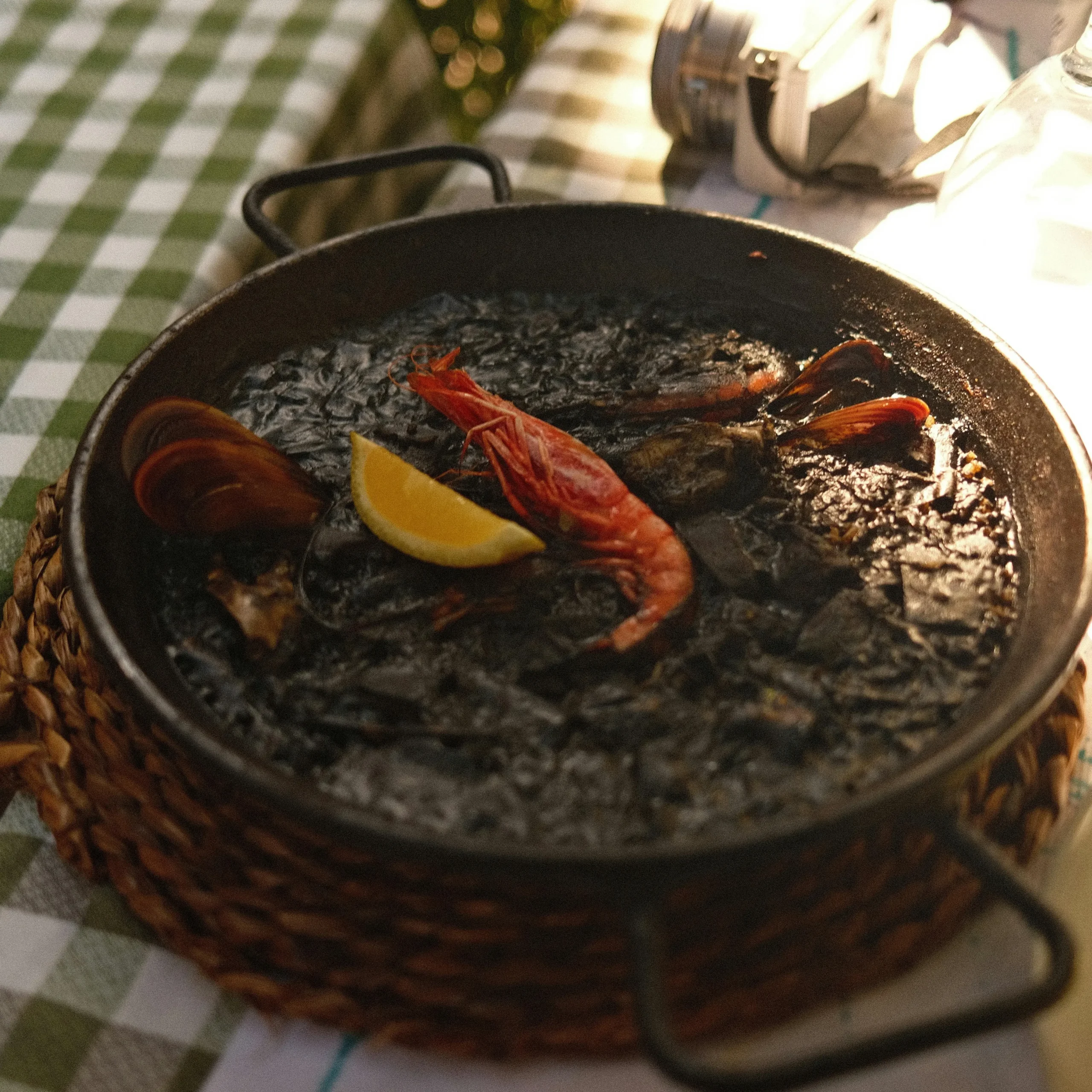 Black seafood paella with prawns, mussels, and lemon wedge served in a traditional pan in Barcelona.