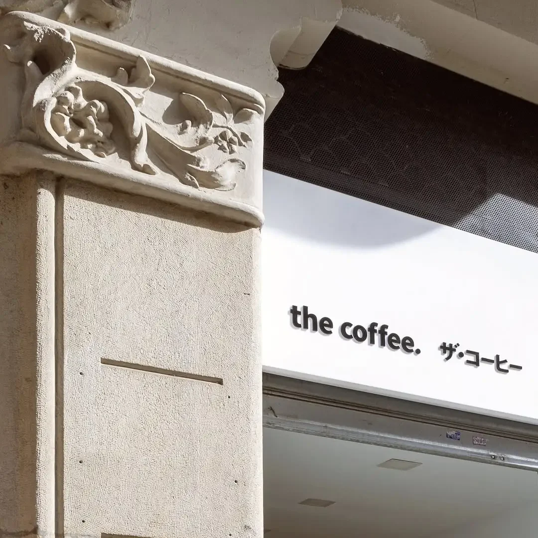 Moderne Fassade von The Coffee in Barcelona, mit einem minimalistischen weißen Schild auf Englisch und Japanisch.