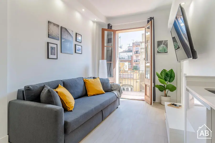 Bright living room with a grey sofa, yellow cushions, wall-mounted TV, and balcony doors opening to a city view.