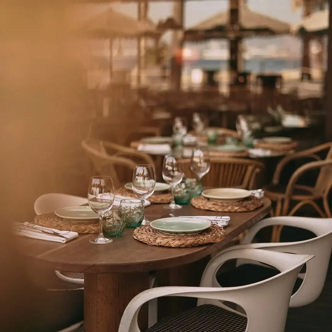 Elegant beachside restaurant table set with ceramic plates, wine glasses, and rustic decor, ready for guests.