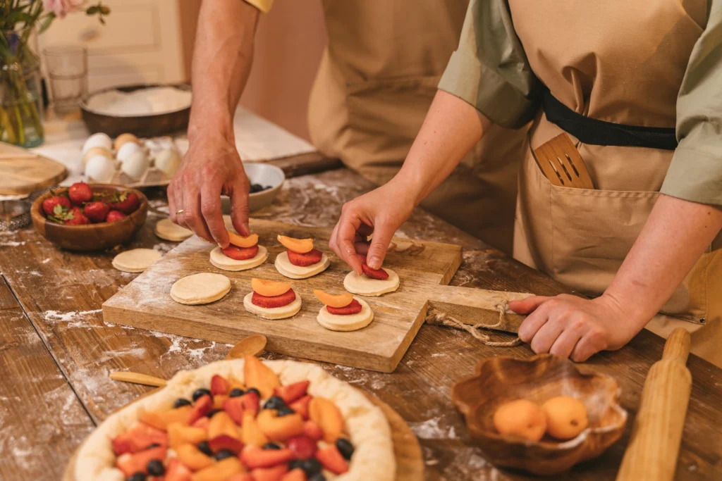 Hands preparing small fruit tarts with strawberries and apricots during a cooking class in Barcelona