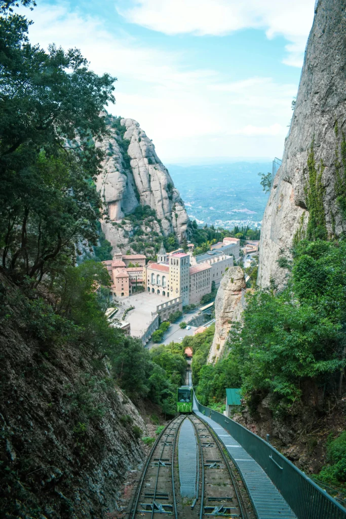 A view of Montserrat Monastery from the funicular railway tracks, with steep cliffs surrounding the area and a clear blue sky in the background