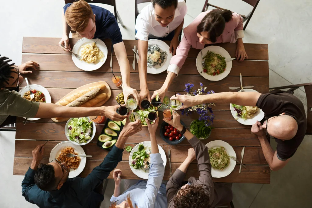 Group of people sitting around a table, sharing a meal and toasting with drinks.