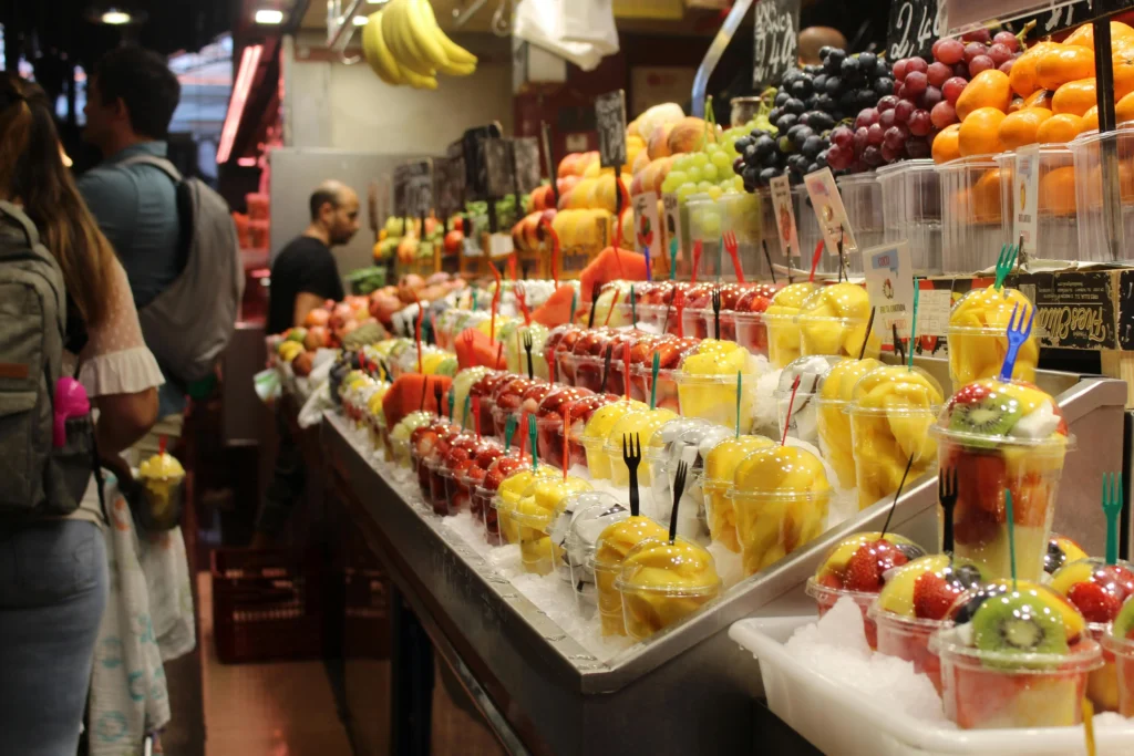 Colorful fruit stalls at La Boqueria Market in Barcelona with fresh juices and cut fruit cups