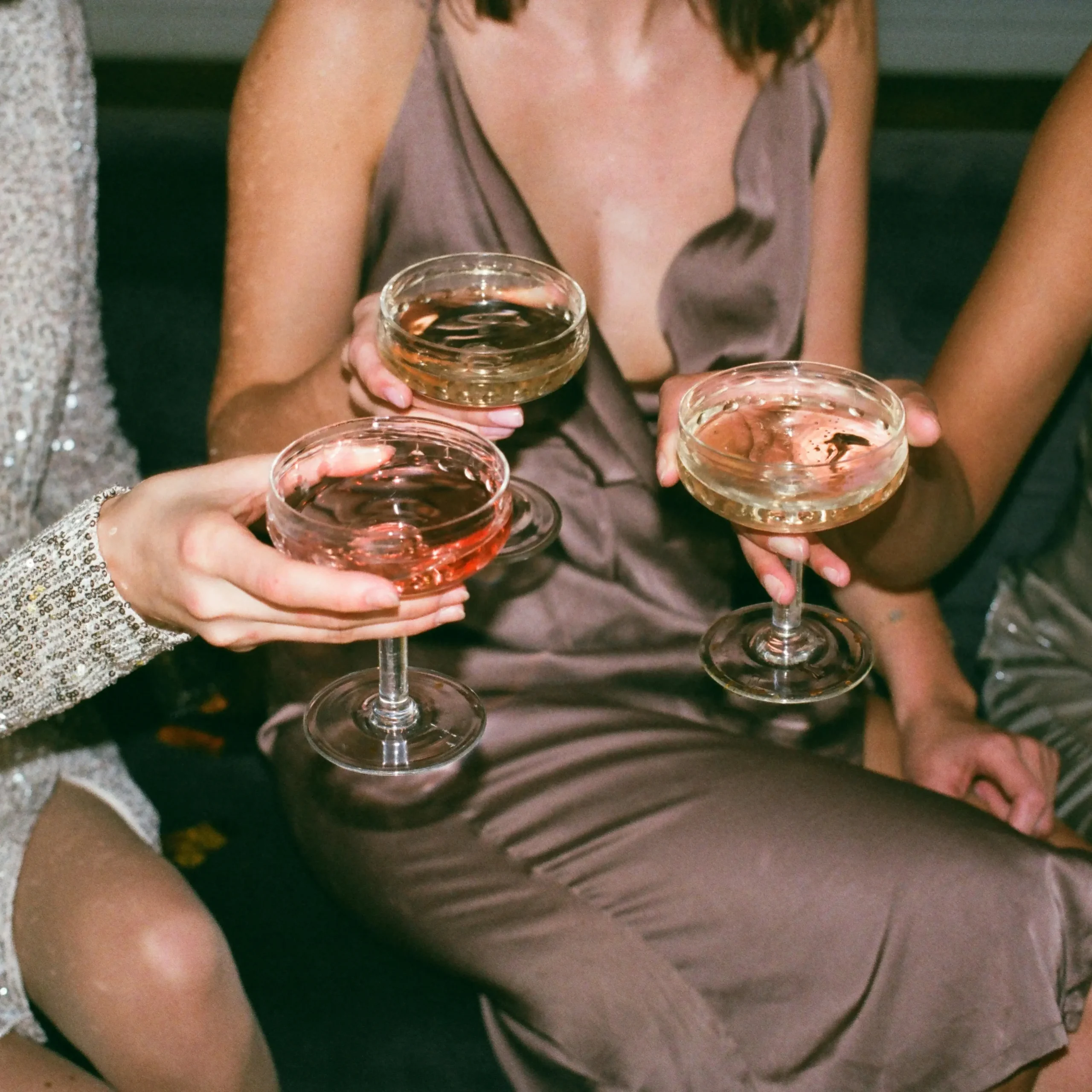 Close-up of three women in elegant dresses holding crystal glasses of champagne and rosé, celebrating together at a festive gathering.