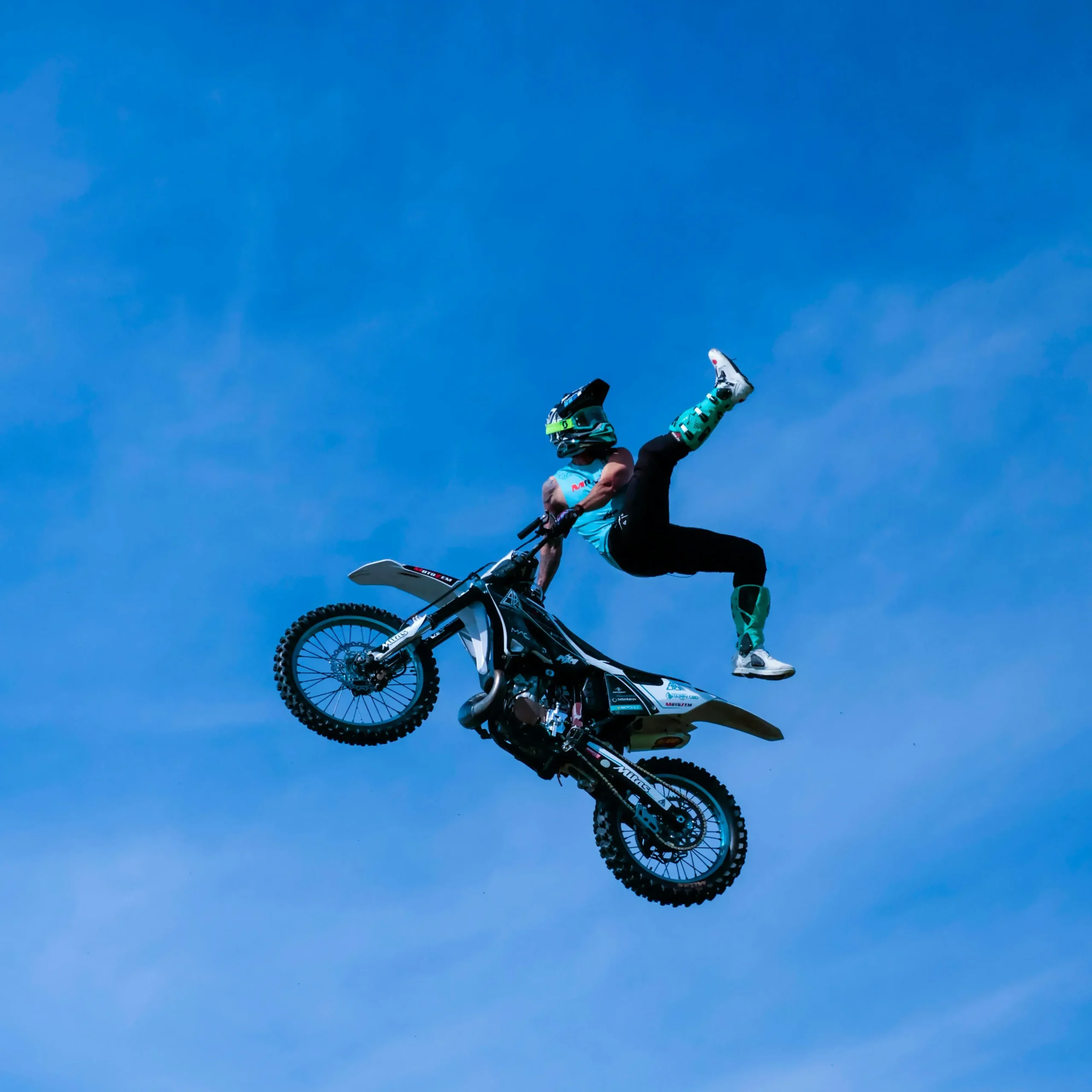 Freestyle motocross rider performing an aerial stunt mid-air against a clear blue sky