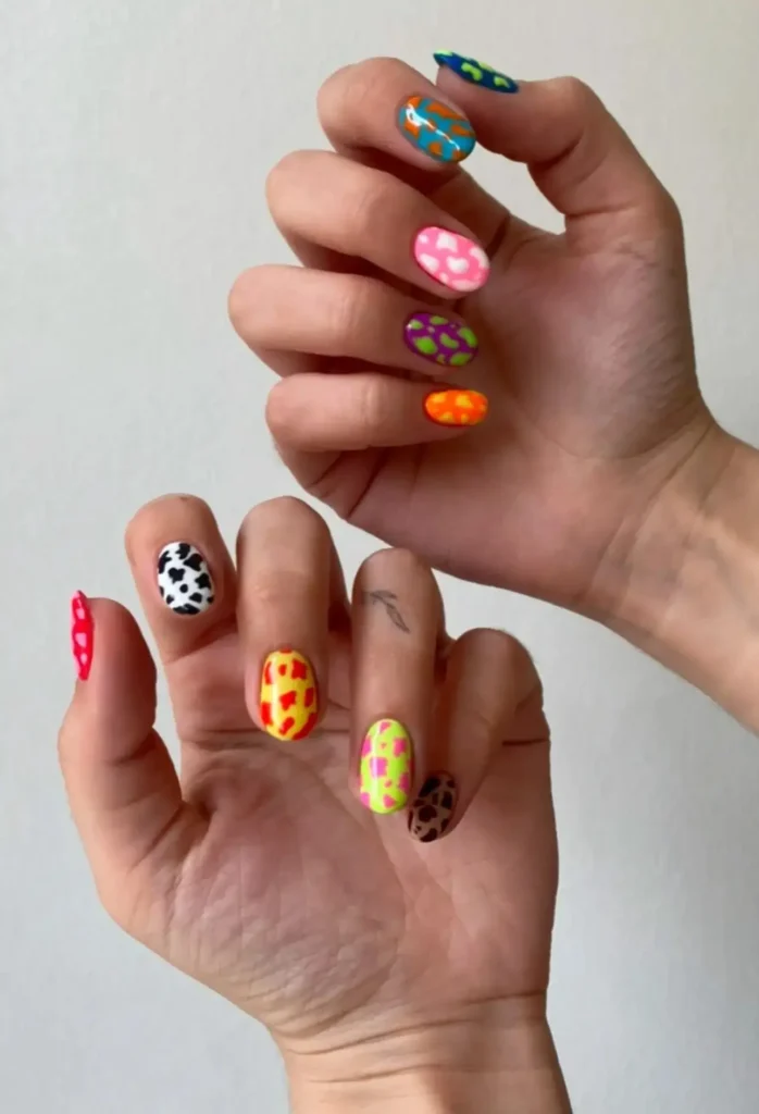 Manos mostrando un diseño de uñas colorido con patrones de animales y colores brillantes como rojo, azul, amarillo, naranja y verde, creando un efecto moderno y atrevido.