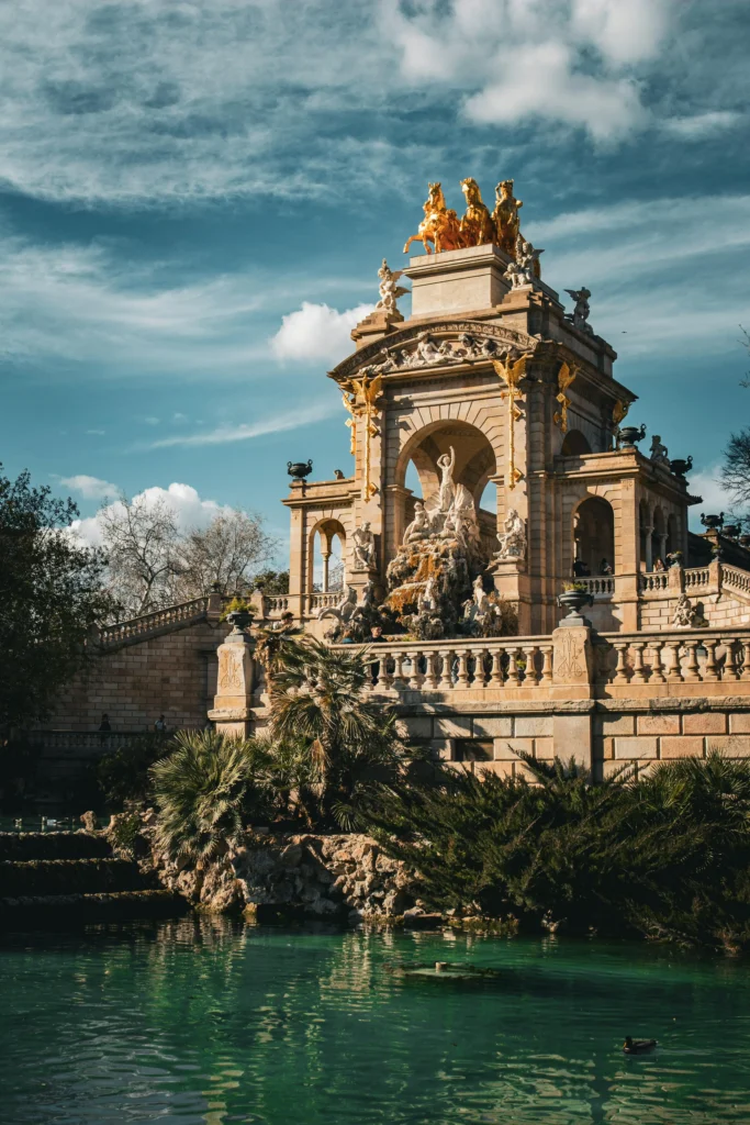 Vista de la majestuosa fuente con esculturas y caballos dorados en el Parque de la Ciutadella, con un cielo azul despejado y vegetación alrededor.