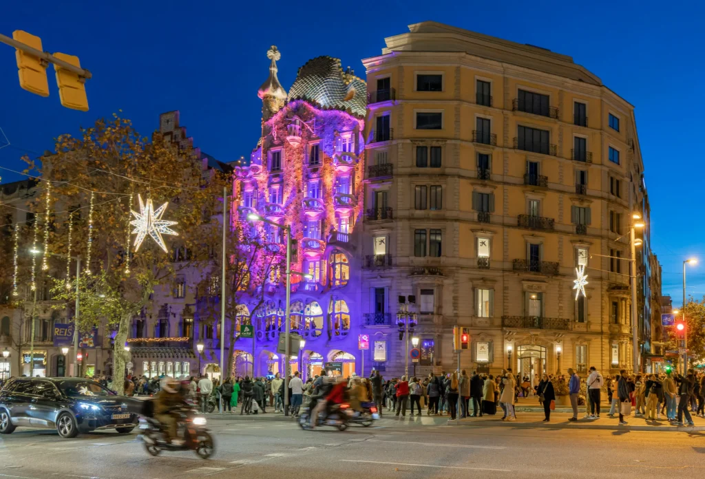 Vista nocturna de la Casa Batlló decorada con luces de Navidad en el Passeig de Gràcia de Barcelona, con gente paseando y tráfico en la calle.
