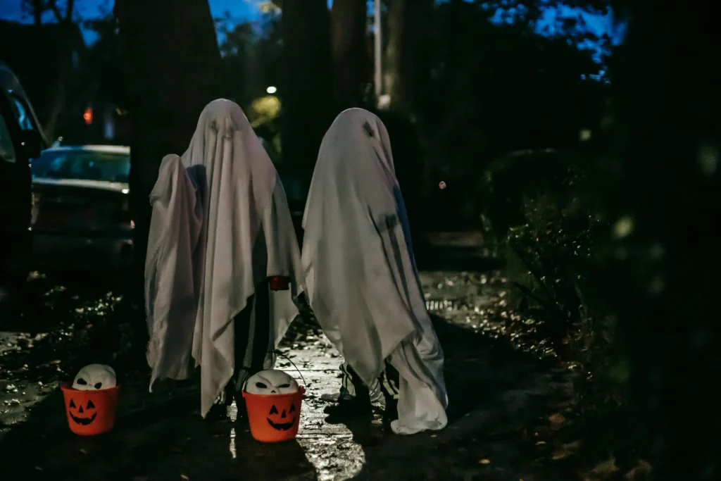 Dos niños vestidos con sábanas de fantasmas durante Halloween, caminando por una calle oscura de Barcelona con calabazas decorativas.