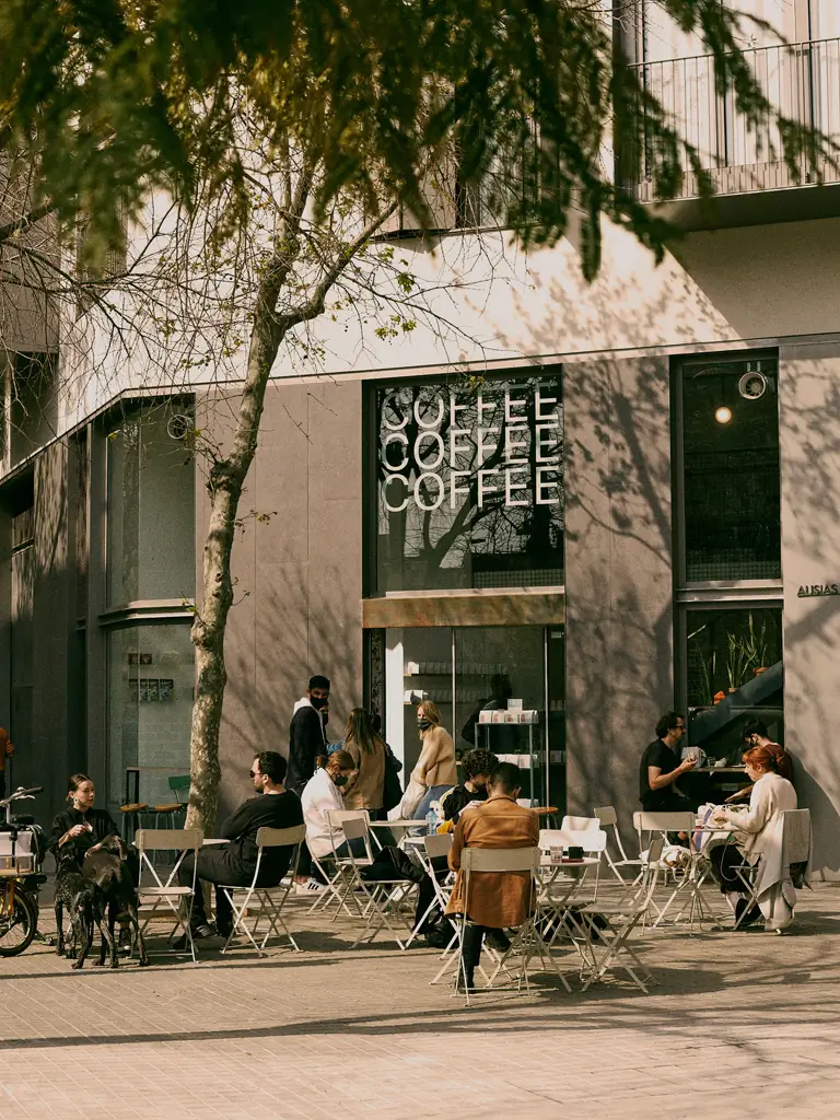 Exterior de Three Marks Coffee con terraza llena de clientes en Barcelona, disfrutando del buen clima y del café en un entorno moderno.
