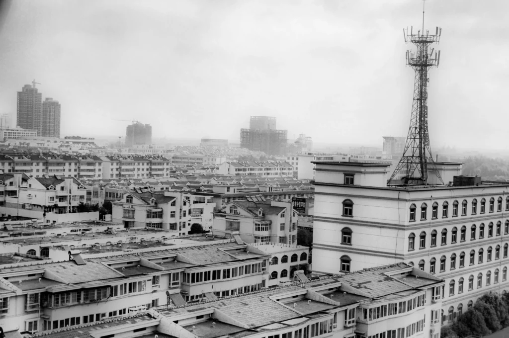 A grayscale cityscape showing a dense urban area with residential buildings and a prominent telecommunications tower on top of a large building in China.