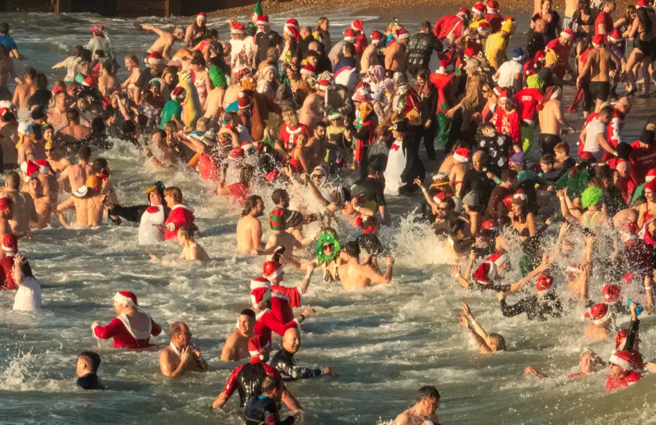 Gran grupo de personas celebrando el tradicional baño de Navidad en la playa, muchas de ellas con gorros y disfraces festivos, disfrutando del agua y del ambiente festivo.