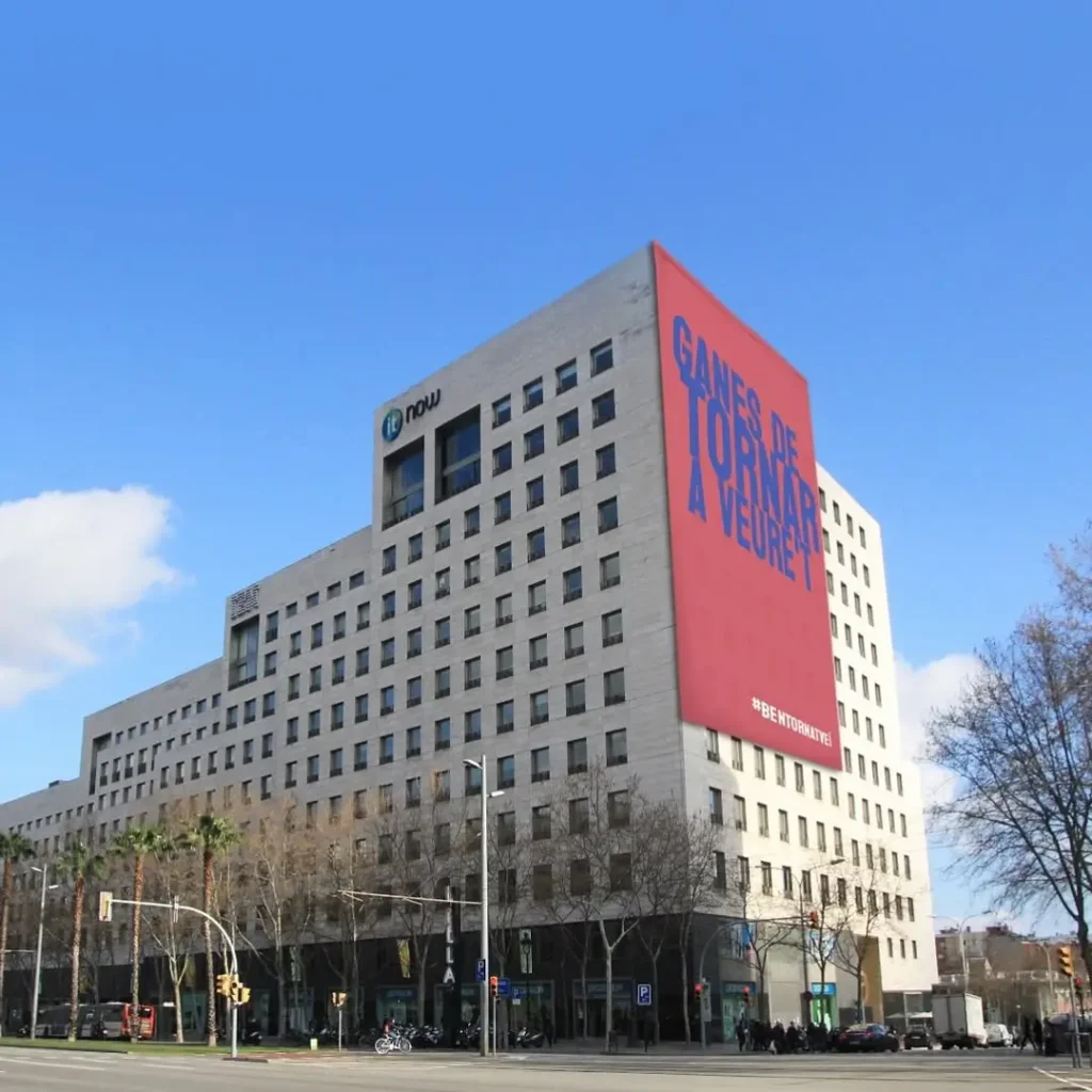 Vista exterior del Centro Comercial Diagonal Mar en Barcelona, con estructuras de cristal azul, escaleras mecánicas de acceso y edificios modernos alrededor en un día soleado.