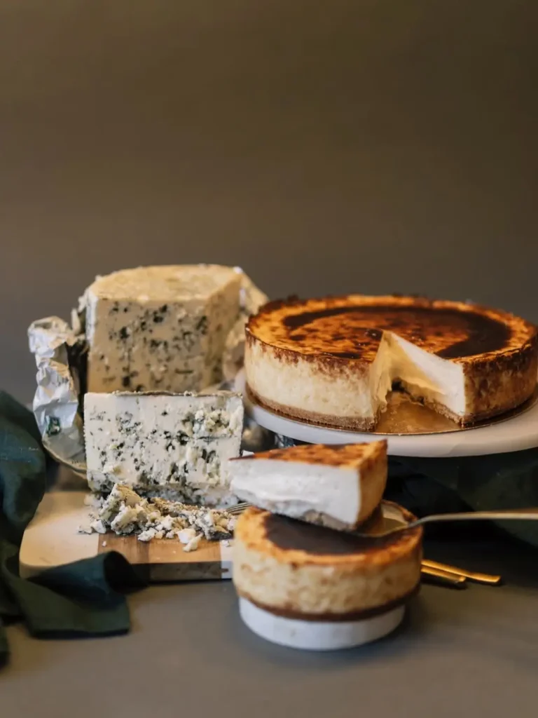 Кремовый чизкейк, поданный с кусочками ручного синего сыра, с мягкой текстурой и золотистой корочкой, представлен на элегантном столе в кондитерской Барселоны.
