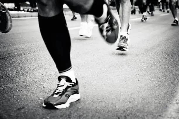 Primer plano de las piernas de varios corredores avanzando por el asfalto durante una carrera urbana, transmitiendo movimiento y energía deportiva.