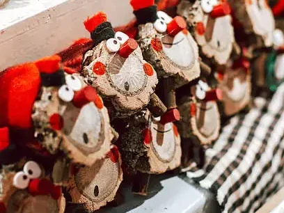 Adornos artesanales navideños con figuras de madera y detalles rojos expuestos en un puesto de mercado, junto a bolas de nieve decorativas, creando un ambiente cálido y festivo.