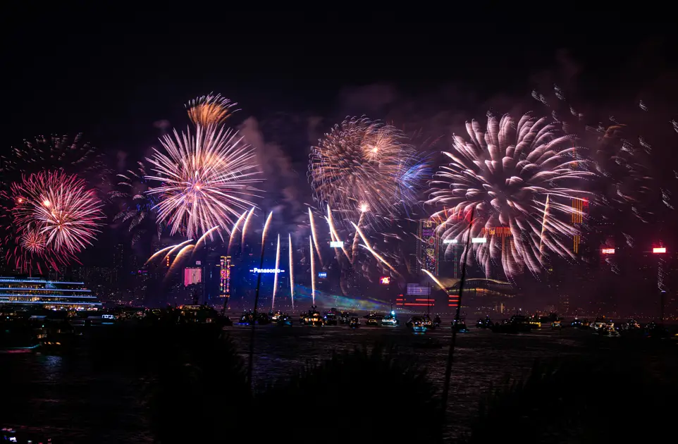 Espectáculo de fuegos artificiales iluminando el cielo nocturno durante la celebración de Nochevieja en Barcelona, con barcos y edificios como telón de fondo.