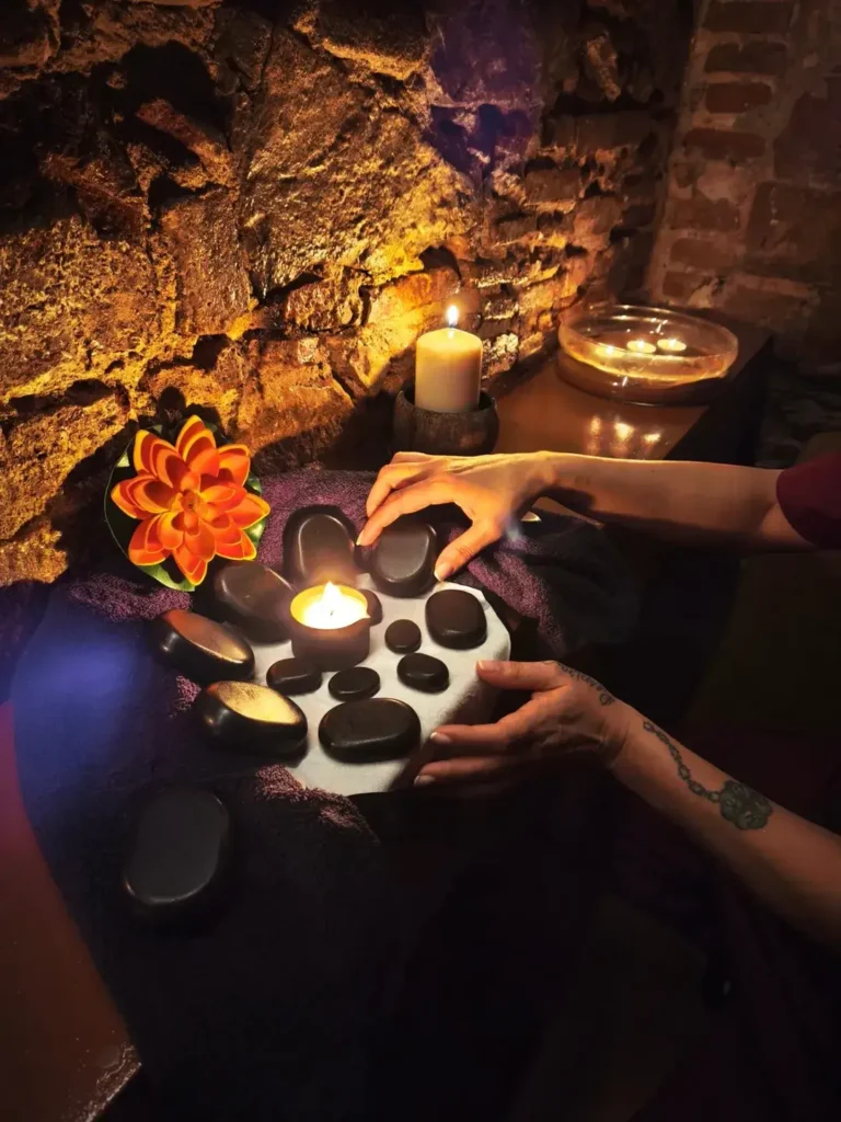 Руки, размещающие горячие камни на полотенце для тела, окруженные свечами и цветами, в спа-атмосфере для оздоровительного лечения.