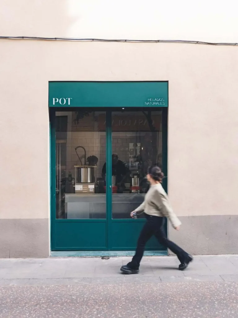 Persona caminando frente a la fachada minimalista verde de POT, una heladería artesanal de helados naturales en Barcelona.