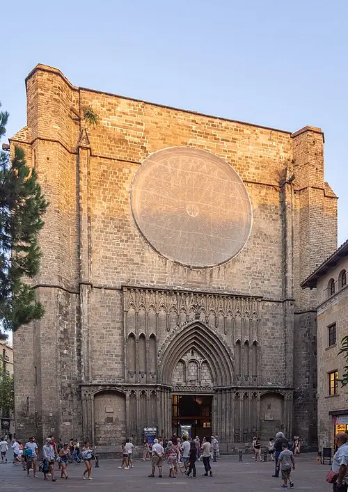 Vista de la Basílica de Santa Maria del Pi en el Barrio Gótico, con su gran rosetón circular, entrada gótica y visitantes caminando por la plaza.