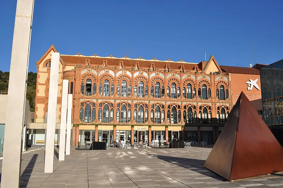 Modernist façade of the CosmoCaixa Science Museum in Barcelona, featuring its red-brick building, large windows, and the open plaza under a clear sky.