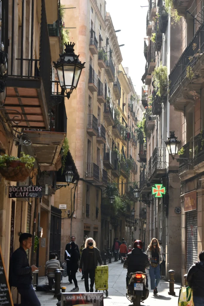 Calle estrecha del centro histórico de Barcelona en invierno, con edificios antiguos, balcones, farolas tradicionales y personas paseando.
