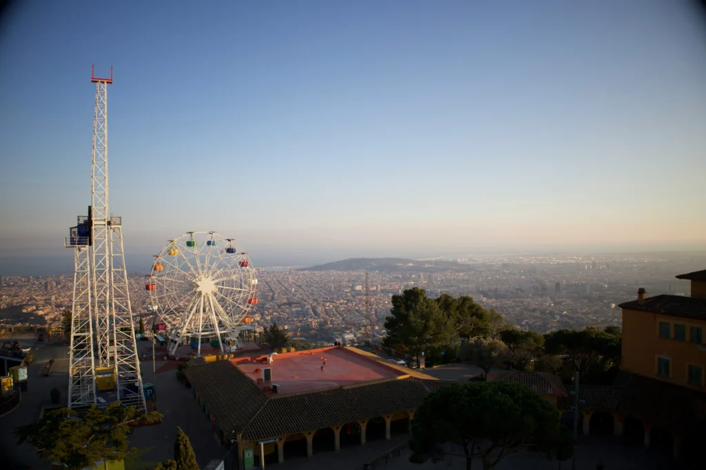 Vista del parque de atracciones del Tibidabo con su noria de colores y estructuras clásicas, contemplando la ciudad de Barcelona al atardecer desde lo alto de la montaña.