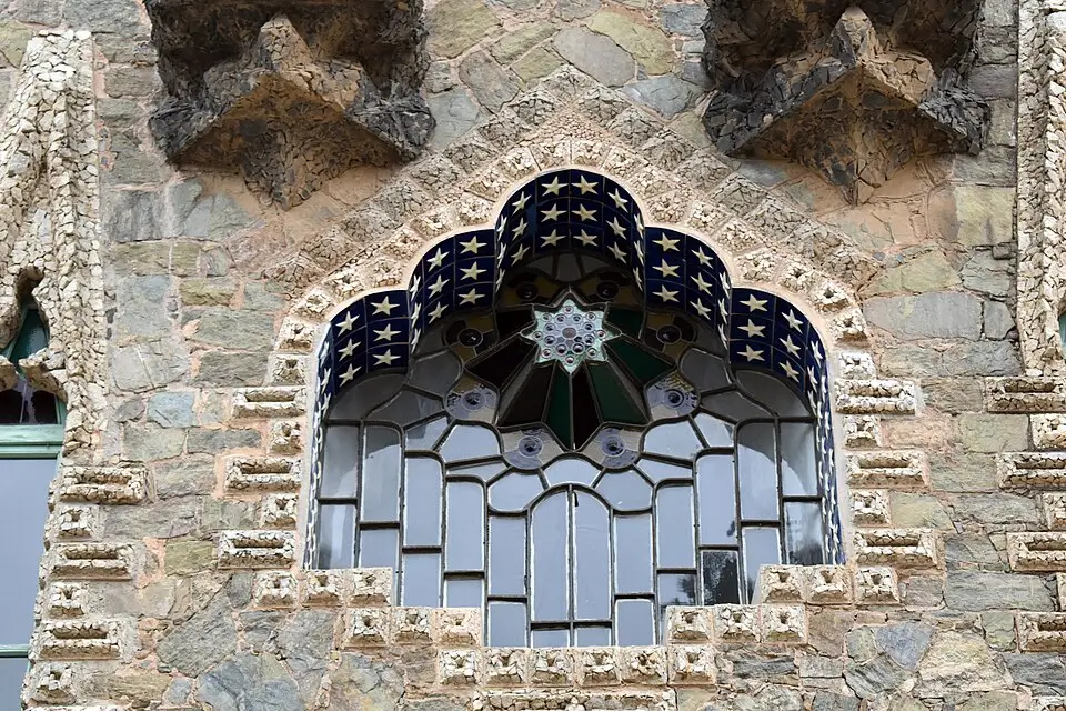 Modernist window of Gaudí’s Bellesguard Tower, decorated with blue mosaic stars and geometric stained glass set into a stone façade.