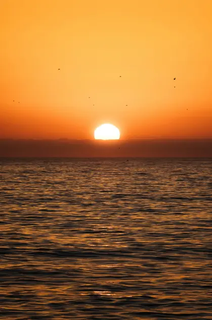 Salida de sol sobre el mar Mediterráneo con el sol en el horizonte y tonos cálidos reflejados en el agua frente a la costa de Barcelona